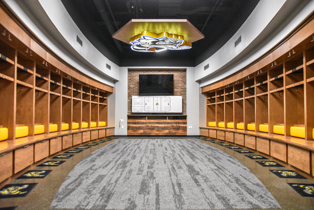 Hockey dressing room with warm woods, and yellow and black accents.